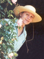 Photograph of Eva Cassidy wearing a hat, peeking out from behind a rosebush